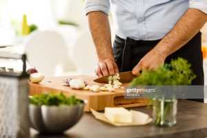 Chef slicing garlic on cutting board in the kitchen, preparing meal.